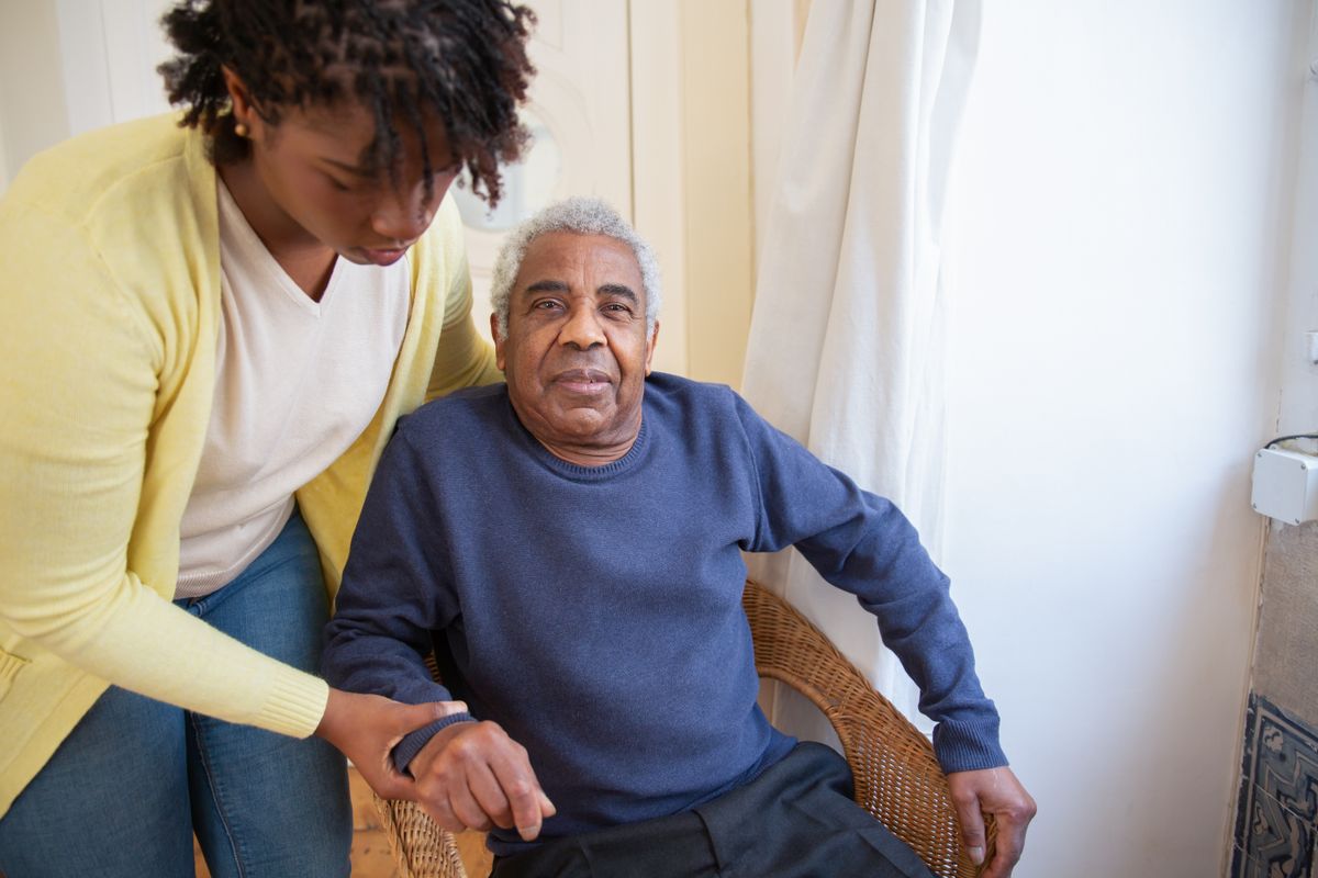 A caregiver helping an older man stand at home